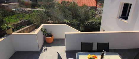 A balcony with a table set for two, a potted plant, and a view of the surrounding area.