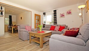 A modern living room with grey sofas, a wooden coffee table, and red cushions. There is a dining area with a wooden table and chairs, and a bookshelf filled with books. - Apartment Milenka (Konavle)