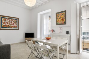 Un coin repas avec une table blanche, des chaises et un téléviseur. Deux tableaux sont accrochés aux murs.