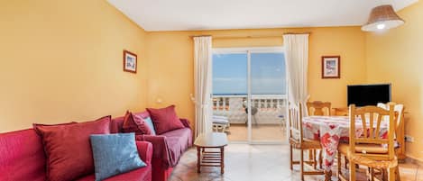 Un salon comprenant un canapé, une table, des chaises, un téléviseur et un balcon avec vue.