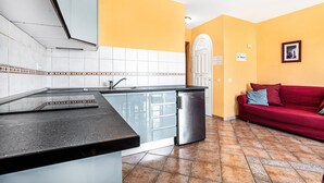 A kitchen with a sink, a refrigerator, and a red sofa in a room with yellow walls and tiled flooring. - Lovely Apartment Close to the Beach with Terrace & Wi-Fi (Costa Calma, Fuerteventura)