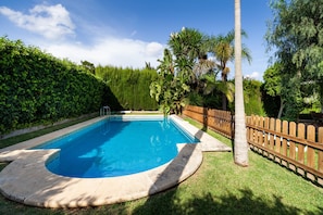 Une piscine dotée d’une terrasse en bois, entourée d’une clôture en bois et d’une végétation luxuriante.