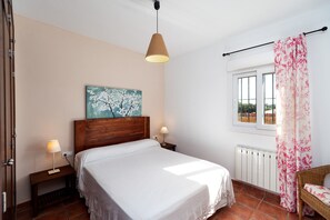 Une chambre à coucher avec un lit, des lampes de chevet, une tête de lit en bois, une fenêtre avec des rideaux et un radiateur.