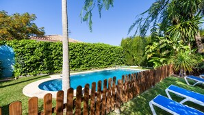 A swimming pool with a wooden fence, surrounded by lush greenery and a clear blue sky. - Holiday Home "La Buganvilla" For Families With Garden and Large Pool (Conil de la Frontera)