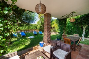 Une terrasse avec des meubles en bois, un pilier en briques et un luminaire suspendu.