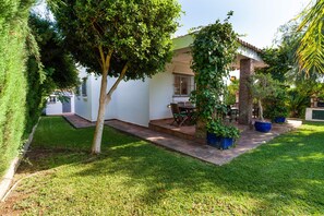 Un jardin bien entretenu, avec une terrasse, un bâtiment blanc et un arbre.