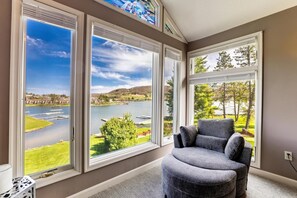 A room with large windows offering a view of a lake, a grassy area, and trees.