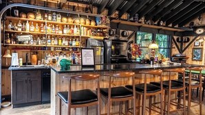 Eine rustikale Bar mit Holzböden, Regalen voller Flaschen, einer Kaffeemaschine und Barhocker.