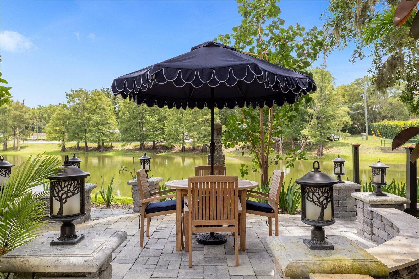 A patio with a table and chairs, surrounded by stone lanterns and a view of a lake.