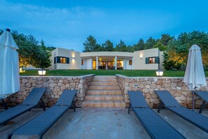 A modern house with a stone staircase leading to a covered entrance, surrounded by a well-maintained lawn and trees.