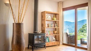 Ein Wohnzimmer mit einer großen Vase, einem kleinen schwarzen Herd, einem Holzbücherregal und einer Glastür, die zu einem Außenbereich führt.