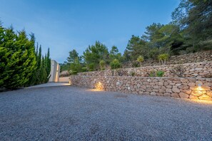 A gravel driveway leading to a stone wall with a modern building in the background.