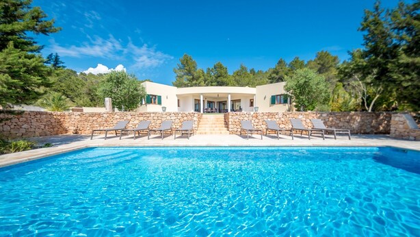 Ein Pool mit Liegestühlen, eine Steinmauer und ein Gebäude mit überdachter Terrasse.