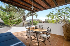 A covered patio with a wooden table and chairs, surrounded by plants and a view of the landscape. - Rural Apartment "Pancho" with Patio, Volcano Views & Wi-Fi (Vegueta Lanzarote)