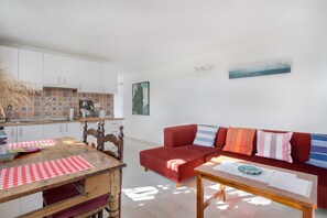Ein Wohnzimmer mit einem roten Sofa, einem Holztisch und einer Küchenzeile mit weißen Schränken und gemusterten Fliesen.