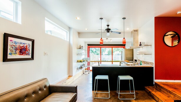 A modern kitchen with a red accent wall, a ceiling fan, and a large window.