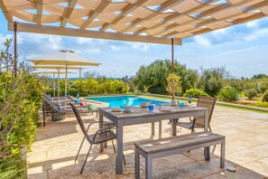 Un patio al aire libre con piscina, una pérgola de madera y una mesa lista para comer.