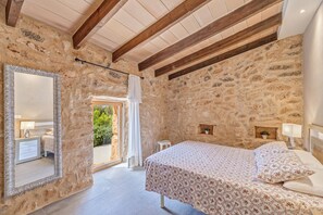 Un dormitorio de paredes de piedra con cama, espejo y una mesita.