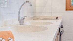 Uma cozinha moderna com azulejos brancos, uma pia de aço inoxidável e uma janela.