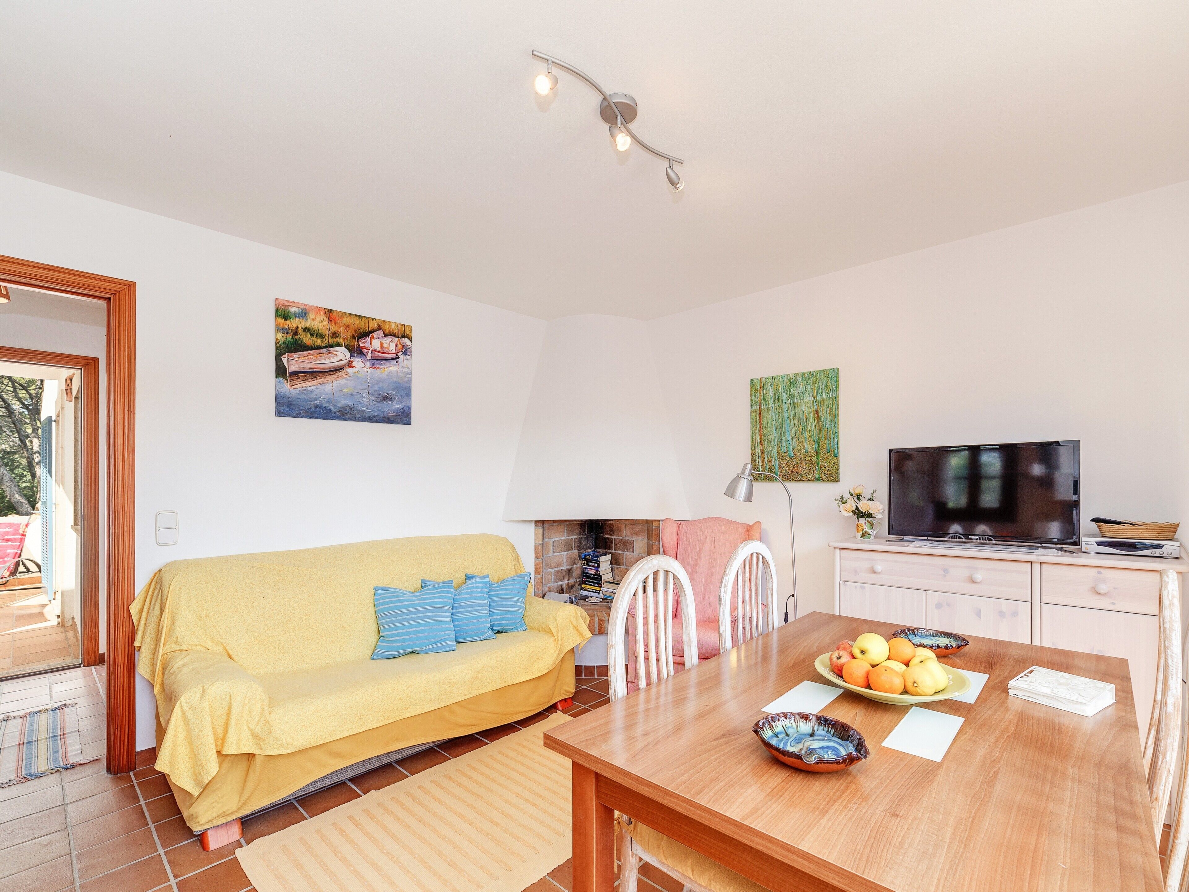 A cozy living room with a sofa, dining table, chairs, a television, and artwork on the walls.