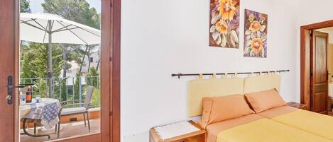 Ein Schlafzimmer mit einem Bett, einem Nachttisch, einem Holzschrank, einem Balkon mit Tisch und Stühlen sowie zwei floralen Bildern an der Wand.