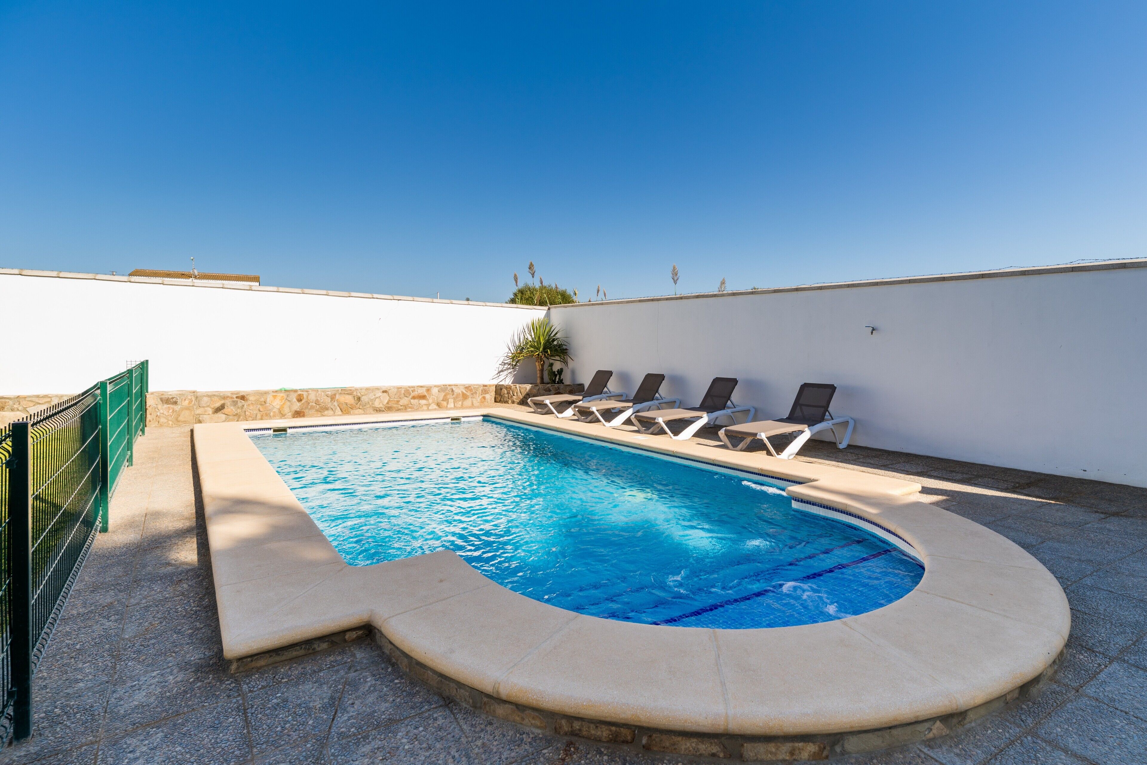 Una piscina de borde curvo, sillones de descanso y un muro de piedra.