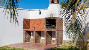 A brick-built outdoor grill with a chimney, set against a white wall with a stone base, under a clear blue sky. - Holiday Home "Villa CA1" with Pool, Garden, Terrace and Wi-Fi (Conil de la Frontera)