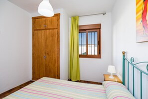 Een slaapkamer met een bed, een houten garderobe, een raam met gordijn, een nachtkastje met lamp, en een metalen hoofdbord.