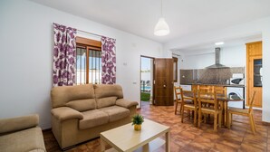 A living room with a sofa, a coffee table, and a dining area with chairs and a table. - Holiday Home "Villa CA1" with Pool, Garden, Terrace and Wi-Fi (Conil de la Frontera)