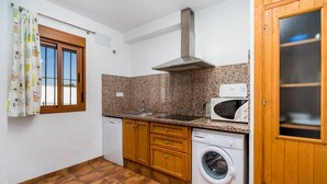 A compact kitchen with a washing machine, microwave, and wooden cabinets. - Holiday Home "Villa CA1" with Pool, Garden, Terrace and Wi-Fi (Conil de la Frontera)