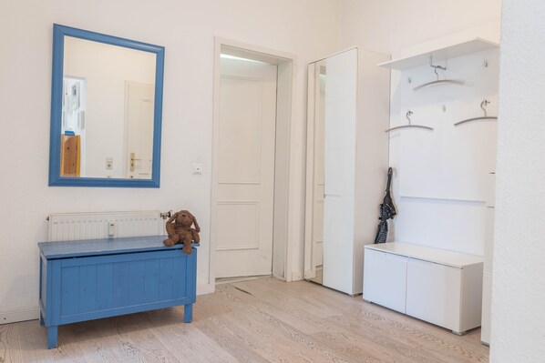 Una habitació amb una banca blava, un mirall, una porta blanca i un penjador.