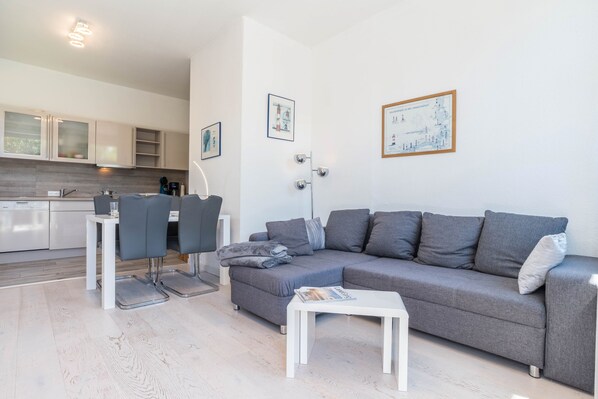 A modern living room with a grey sofa, white coffee table, and a dining area with a white table and chairs.