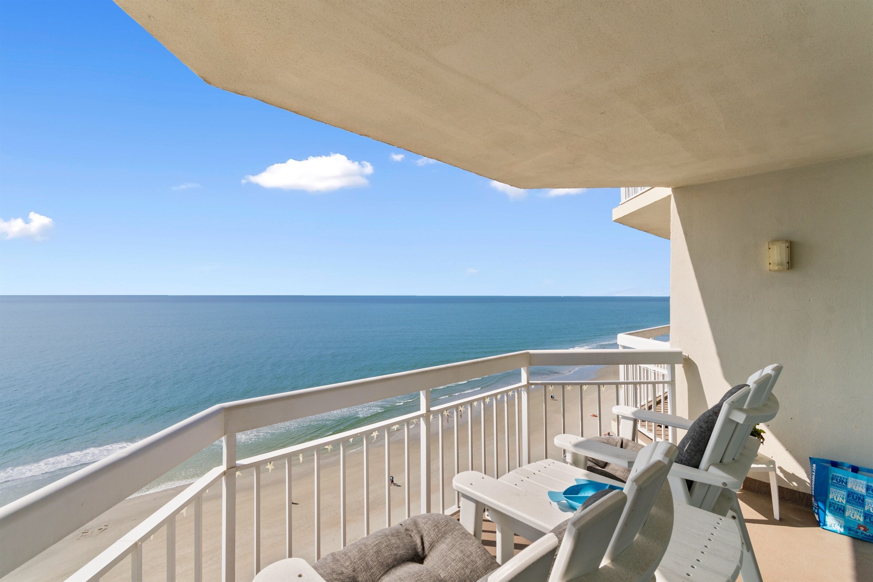 A balcony with a view of the ocean, white chairs, and a small table.