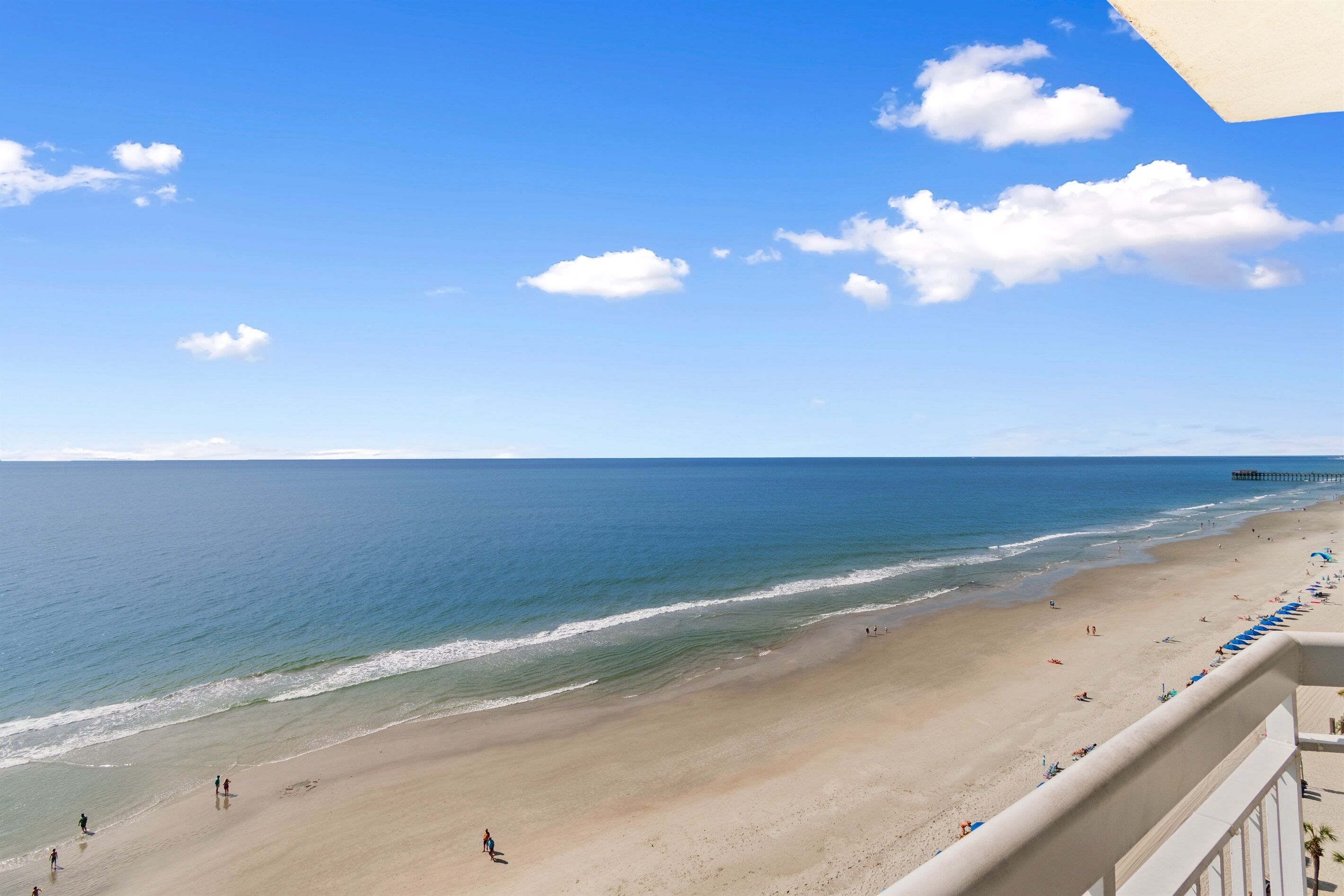 A beach with a pier in the distance, clear skies, and a few people on the sand.