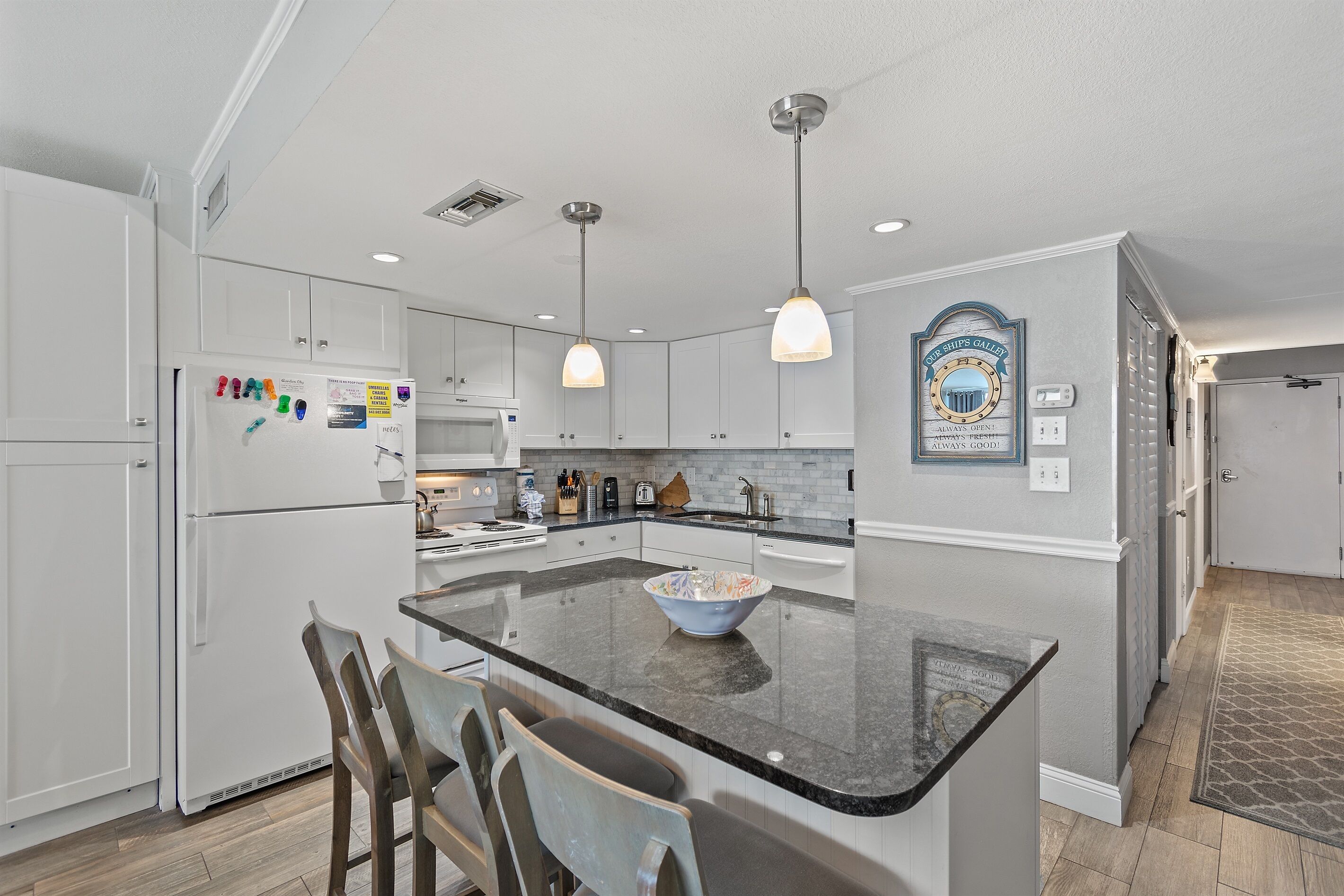 A modern kitchen with white cabinetry, a granite countertop, and pendant lighting.