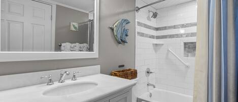 A bathroom with a white sink, mirror, and toilet. There is a shower curtain and a towel rack with towels.
