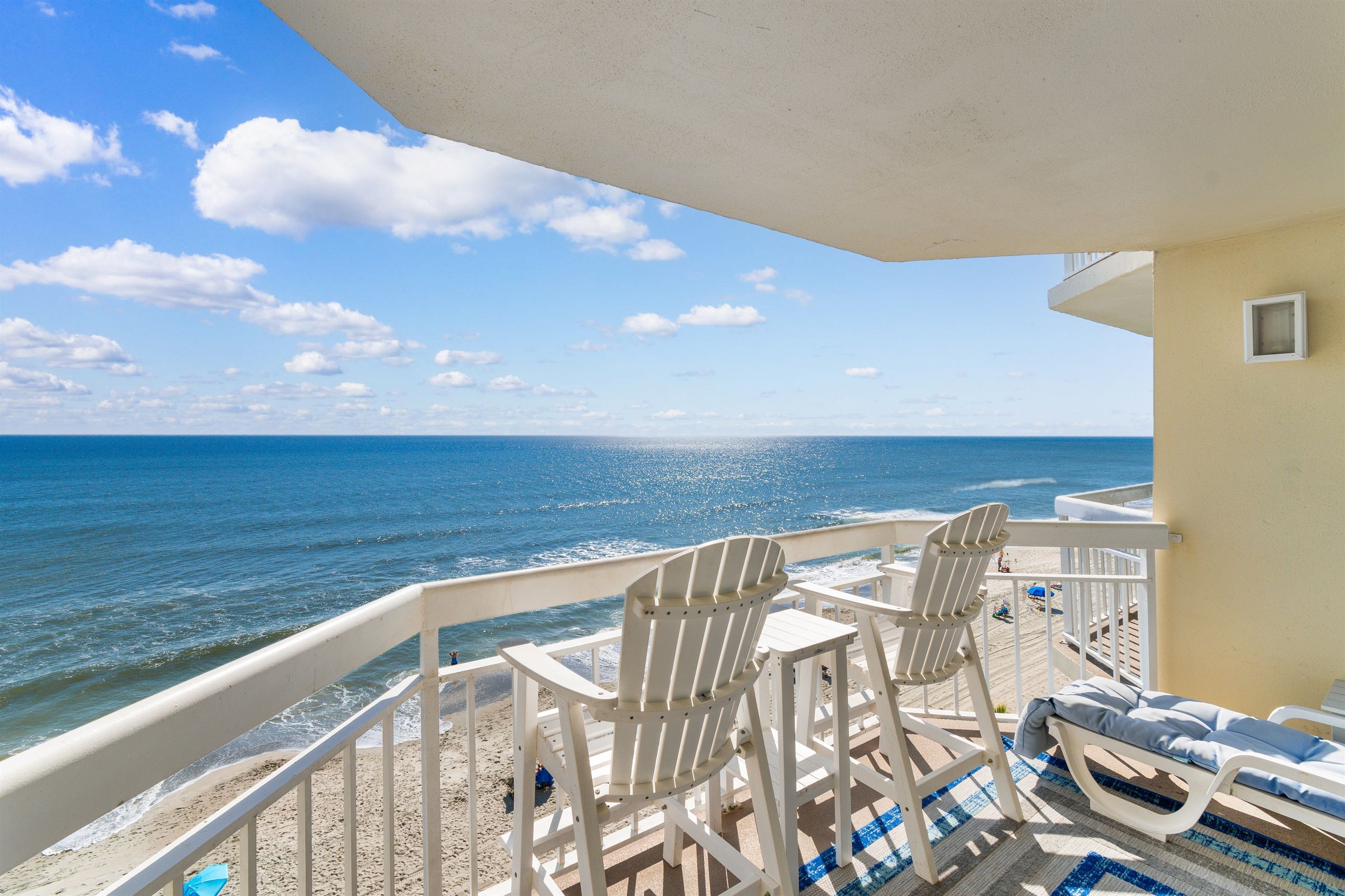 A balcony with two Adirondack chairs and a sun lounger overlooking the ocean.