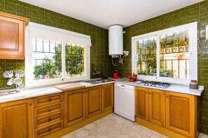 A kitchen with wooden cabinets, a dishwasher, a stove, and large windows with a view of greenery.