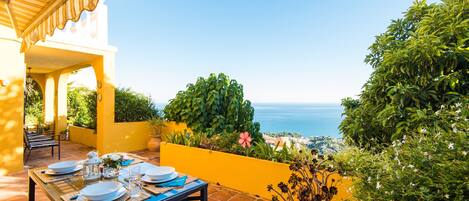 Un espace de restauration en plein air avec une table dressée pour quatre personnes, offrant une vue panoramique sur l’océan.
