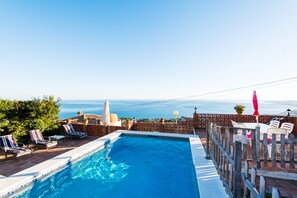 A swimming pool with lounge chairs, a wooden fence, and a view of the ocean.