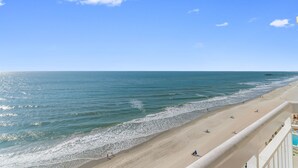 A beach with a clear sky, a sandy shore, and a pier in the distance. - Garden City Beach Oceanfront Condo 910 | Rising Tides Properties Rental (Murrells Inlet)