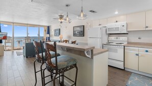 A modern kitchen with a large island, white appliances, and a view to the outside. - Garden City Beach Oceanfront Condo 910 | Rising Tides Properties Rental (Murrells Inlet)