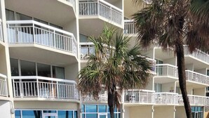 A pool area with a clear view of the ocean, surrounded by a multi-story building with balconies. - Garden City Beach Oceanfront Condo 910 | Rising Tides Properties Rental (Murrells Inlet)