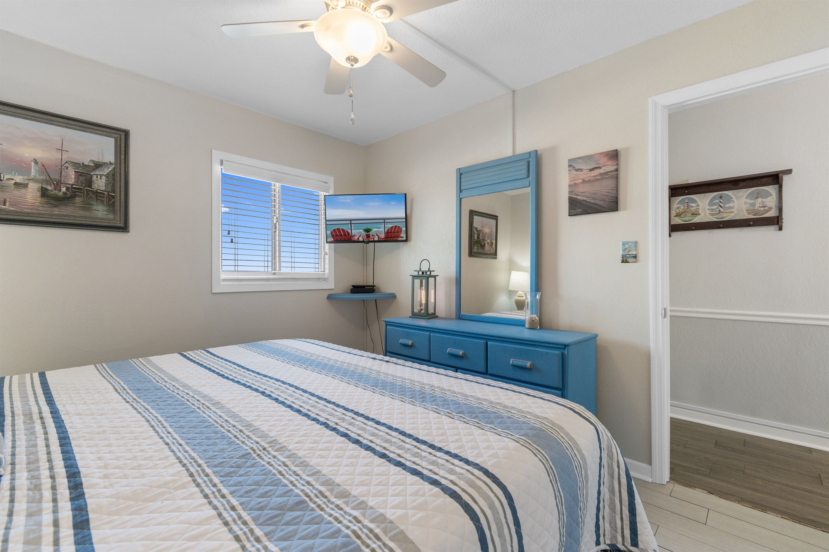 A bedroom with a bed, a ceiling fan, a TV, a dresser, and a window with blinds.