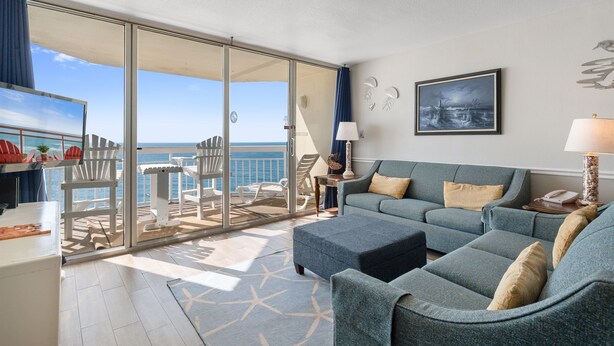 A balcony with a view of the sea, a sofa, a table, and a chair. - Garden City Beach Oceanfront Condo 910 | Rising Tides Properties Rental (Murrells Inlet)