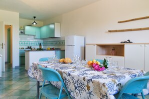 Un coin repas avec une table dressée pour quatre personnes, une cuisine en arrière-plan et une porte donnant sur une autre pièce.