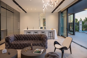 Uma sala de estar moderna com um sofá estofado, uma mesa de centro redonda e um espaço bar com banquetas.