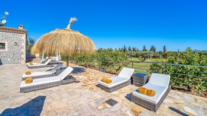 Una terraza en la azotea con suelo de piedra, sillones de mimbre con cojines, un parasol de paja y vistas al campo.