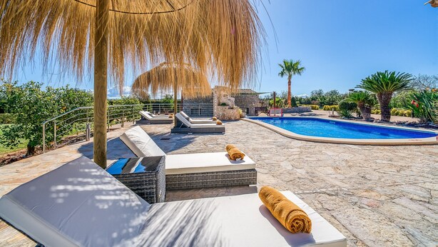 Zona junto a la piscina con sillones, una piscina de piedra y una pérgola que ofrece sombra.