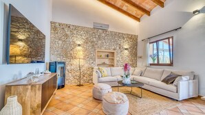 Una sala de estar con pared de piedra, un sofá, otomanas, una mesa de centro y un televisor.